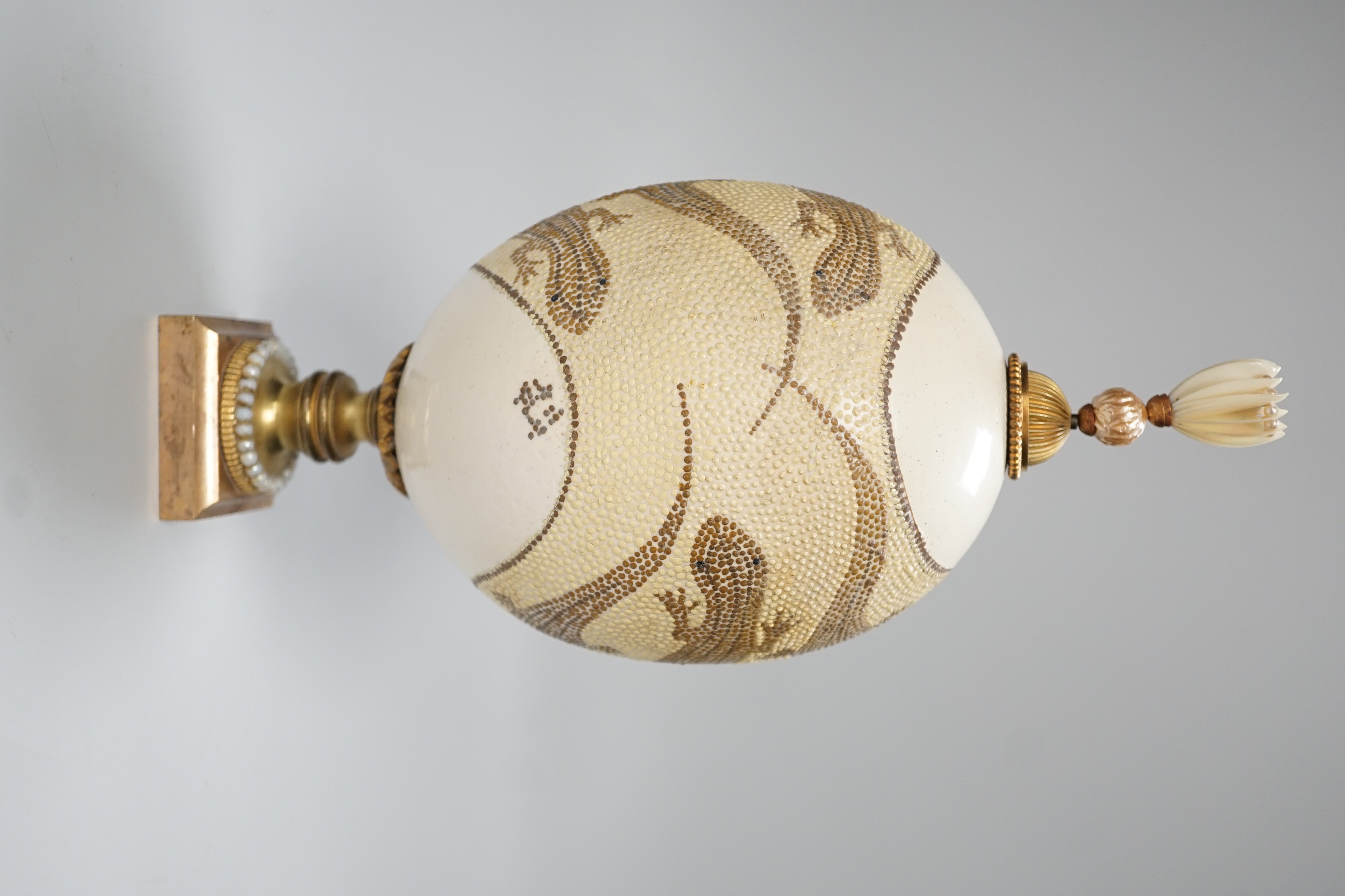 A decorated ostrich egg on gilt stand with a gilt and seed finial, 27cms high